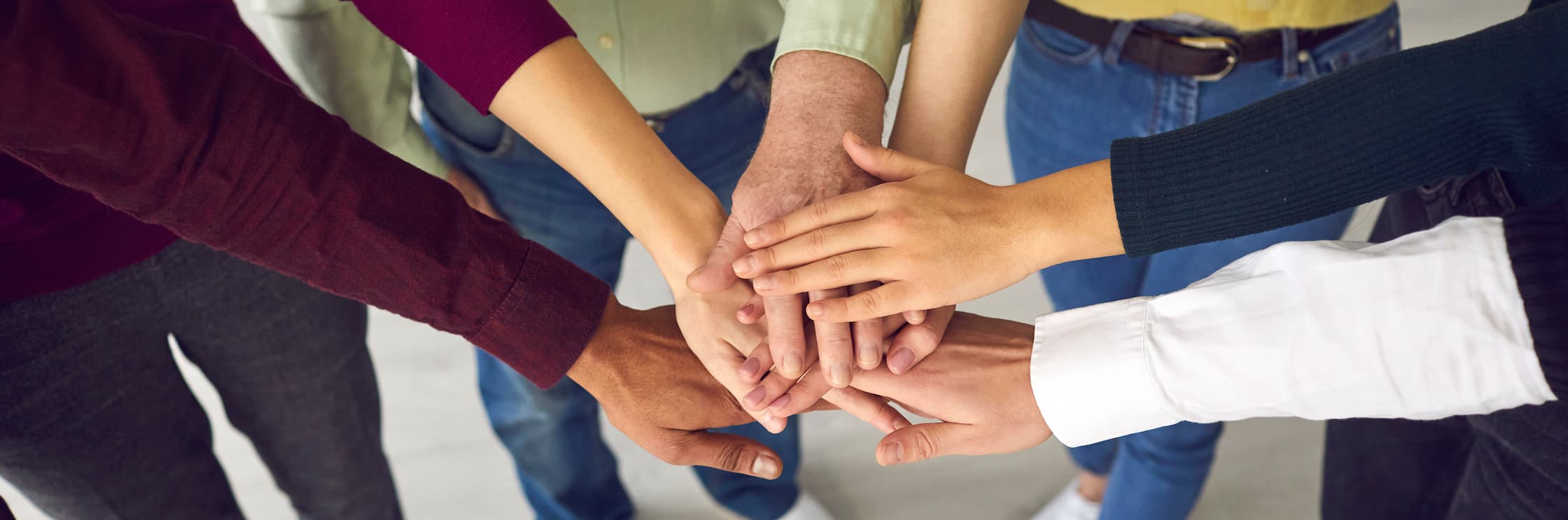 group of people putting hands in a circle on top of each other in cheer format