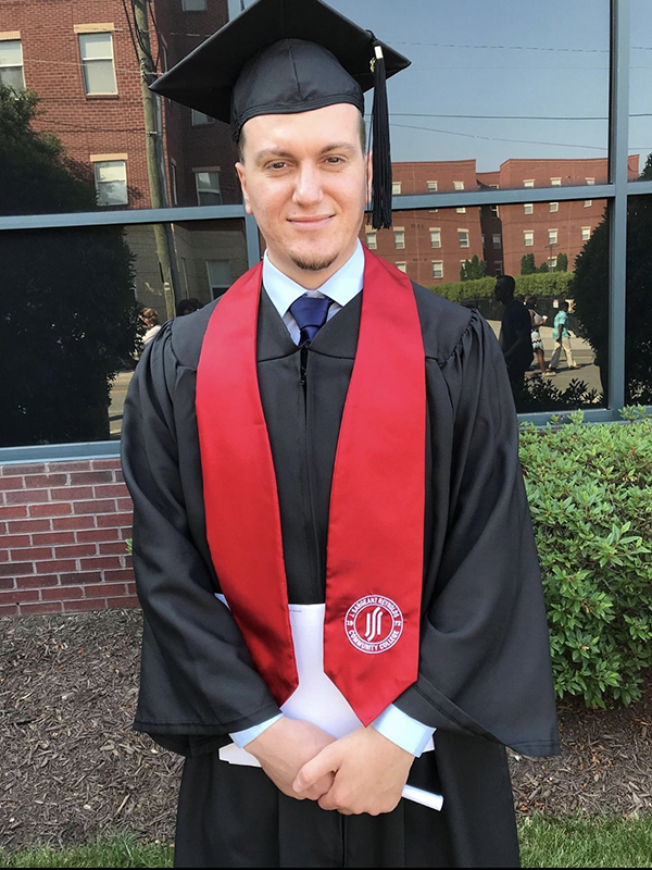 Fitim Xhemaili, young man in gradution regalia smiles for the camera