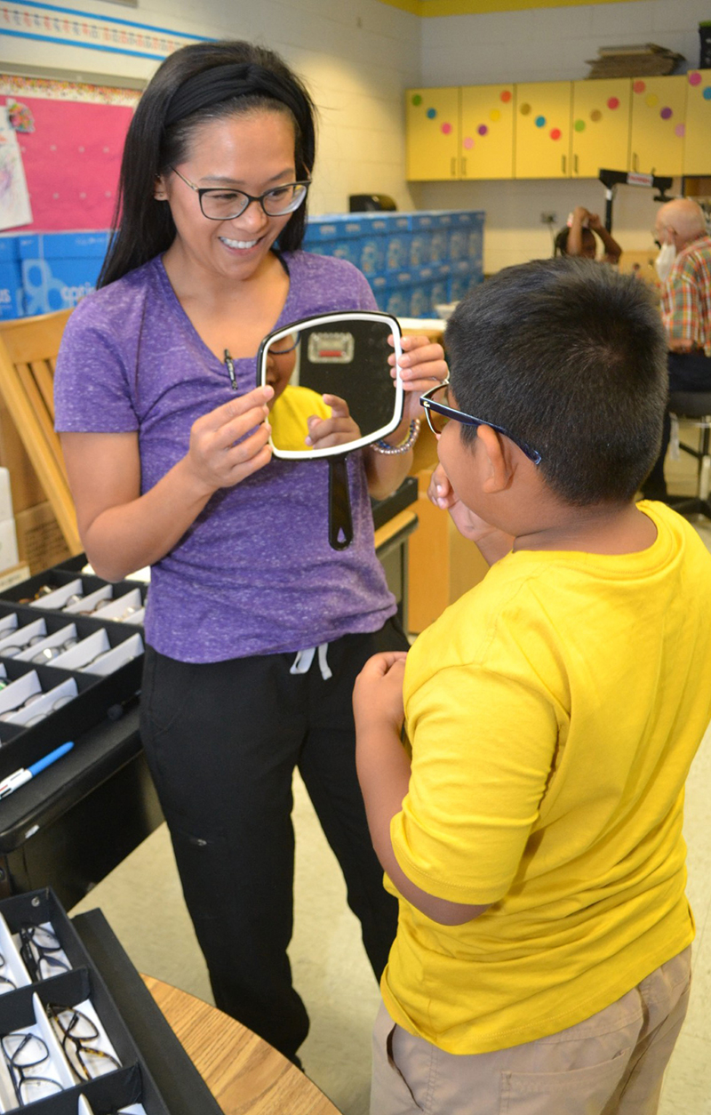 Frankie Lunsford hold mirror for young man who looks at his new glasses