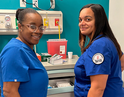 Nursing students, Joliesha Smith and Marissa Roby, wearing blue scrubs pose in front of medical equipment.