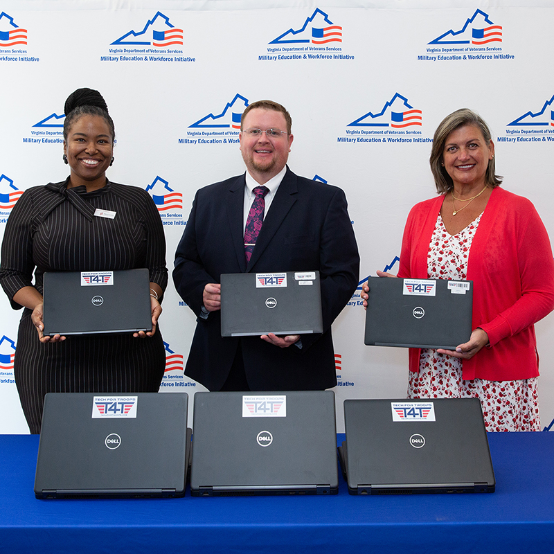 Three people display donated laptops for military students