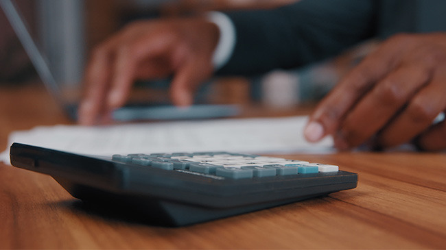 Professional in suit working with a calculator on a desk.