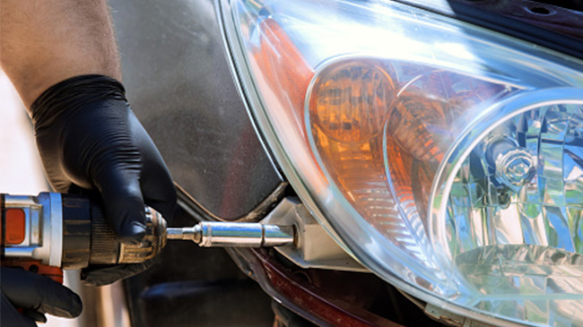 A person wearing black gloves repairs a car headlight using a drill.