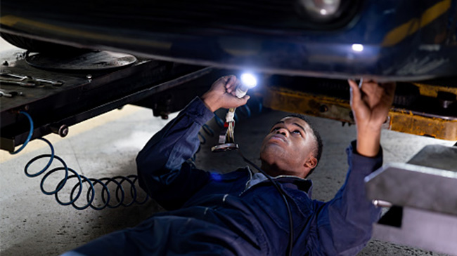 A man fixing a car engine under the open hood, using tools and wearing protective gloves.