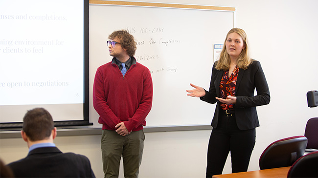 Two individuals standing in front of a whiteboard, presenting a business plan.