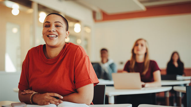 Student smiling during class discussion with classmates seated at desks in the background