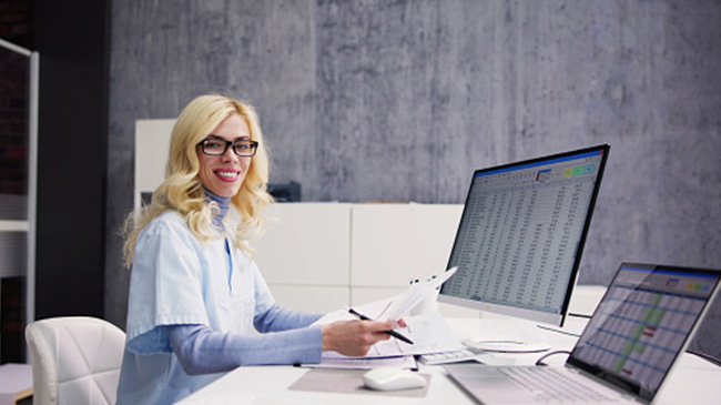 A woman with glasses working on a laptop at a desk.