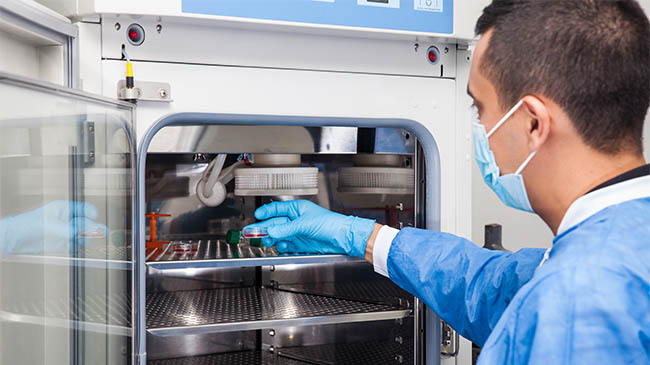 A man in a blue coat and gloves sterilizing surgical equipment 