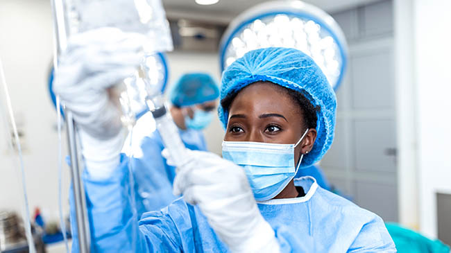 A woman in a surgical gown and blue hat holding a tube