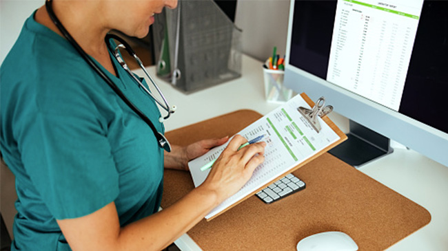 Healthcare professional in scrubs taking notes on a clipboard.