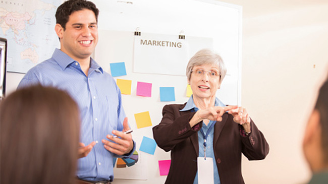 A man and woman standing in front of a white board, discussing a project presentation.