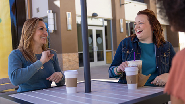 Three women enjoying drinks at a table, engaged in conversation and laughter.