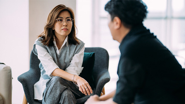 A woman engaged in conversation with a man while comfortably seated in a chair.