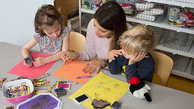 A woman and two children sitting at a table, engrossed in coloring with crayons.