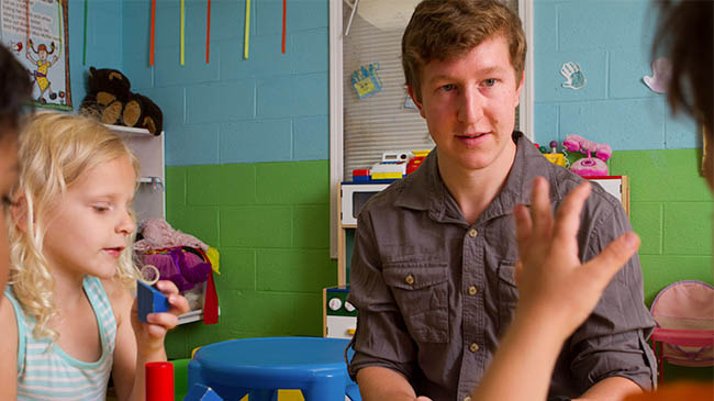 A man and two children sitting in a classroom, engaged in a learning environment.