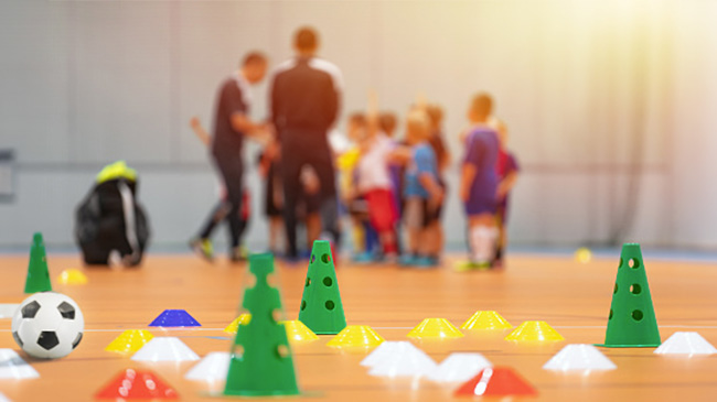 A group of children playing soccer on an indoor court.