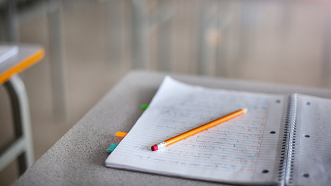 A notebook and pencil on a desk in a classroom.