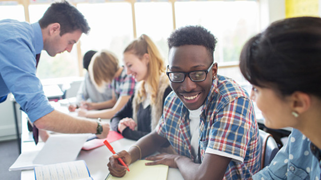 A teacher standing in front of a diverse group of students in a classroom, engaged in a lesson.