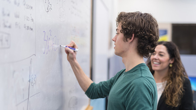 A man and woman collaborating, writing on a whiteboard to exchange ideas and brainstorm together.